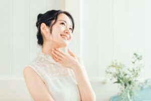 白いドレスを着て首元に手を置く女性